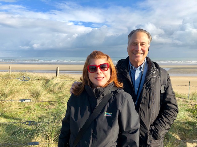 Sheri and Les Biller standing in front of barbed wire in front of a beach